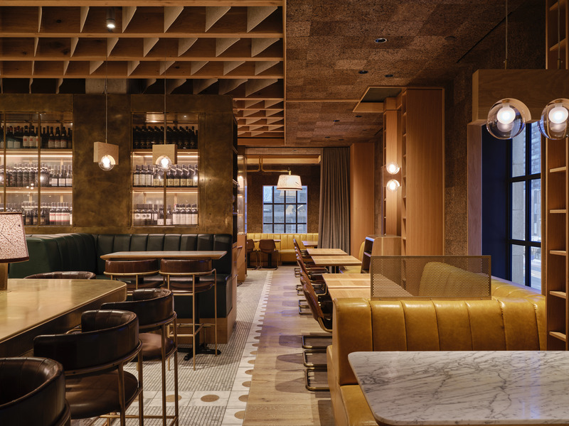 Discrete and tufted golden yellow banquettes, oak shelving and cork walls sit spaced from the original exterior walls to expose the historic windows and city views.
Photo credit: Doublespace