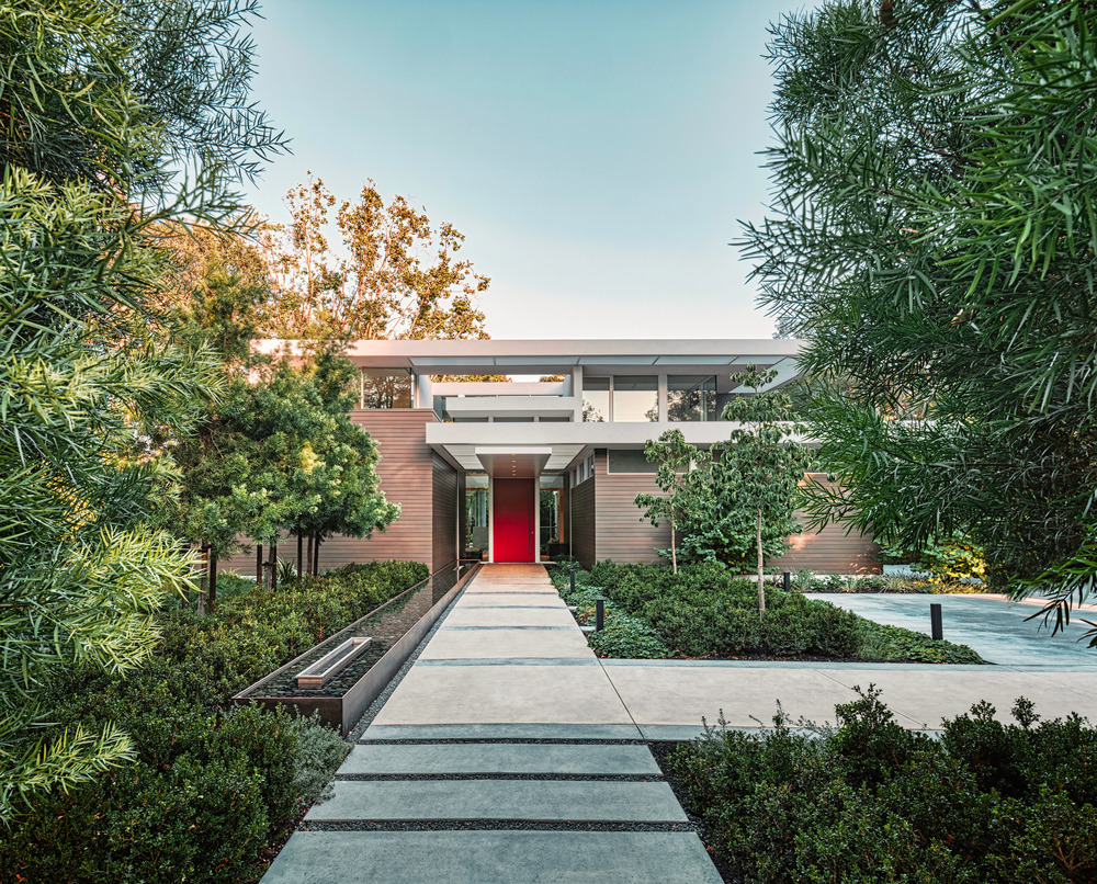 Owyang House: The entry sequence to this new, two-story residence is a study in expansion and compression: The pathway, flanked by a long, linear infinity-edge water feature, opens to the sky, while a long, low steel canopy compresses the exterior entrance space and focuses attention on the dramatically hued entry door.
Photo credit: Tim Griffith