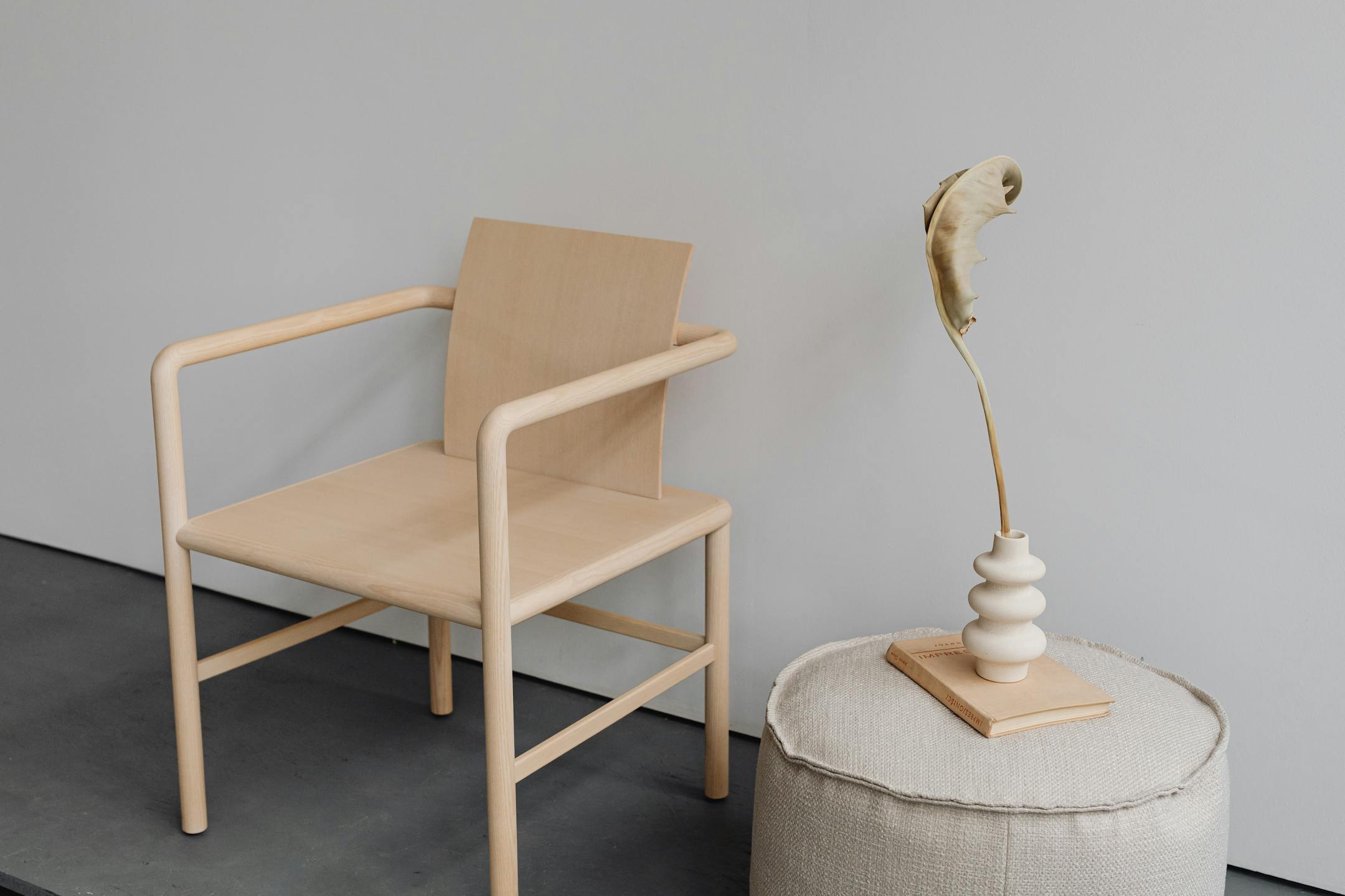 A minimalist wooden chair alongside a modern vase and pouf, showcasing elegant design.