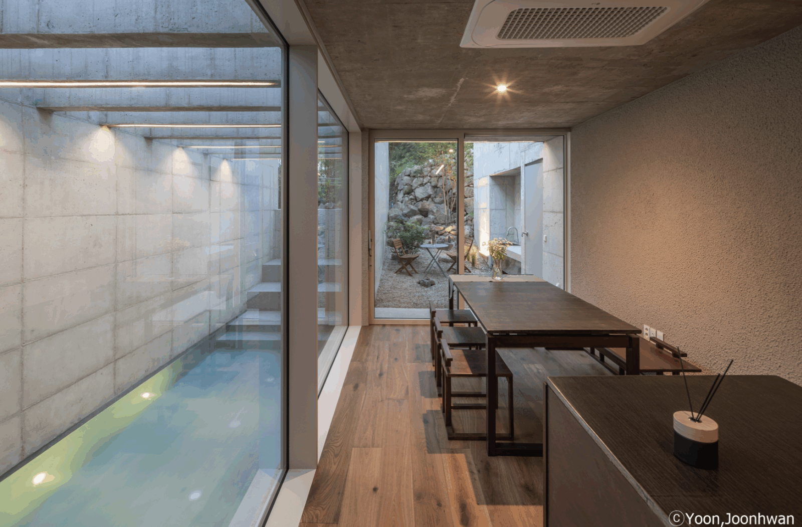 The interior of the Hadong house, showing an indoor pool, a table with chairs and glass walls