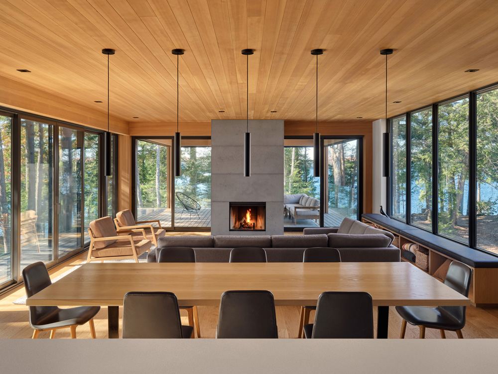 The upper - level living spaces float above the forest, with wrap - around windows and sliding doors opening to a sunlit deck that blurs the line between indoors and out.
