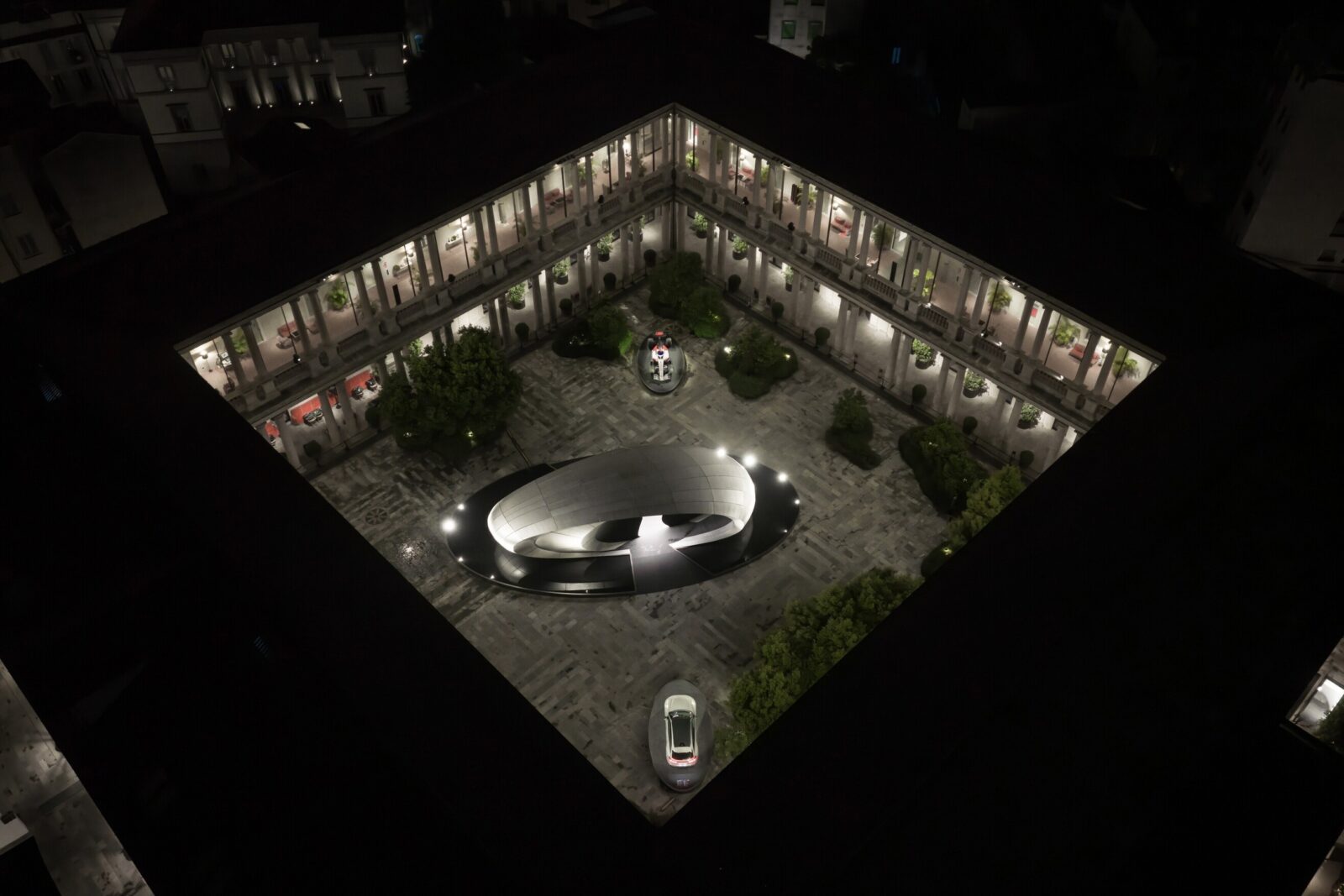 Night-time aerial view of the installation Origin during Milan Design Week 2026. The reduced, oval architectural form contrasts with the historic courtyard architecture, underscoring the approach to design as a cultural dialogue.