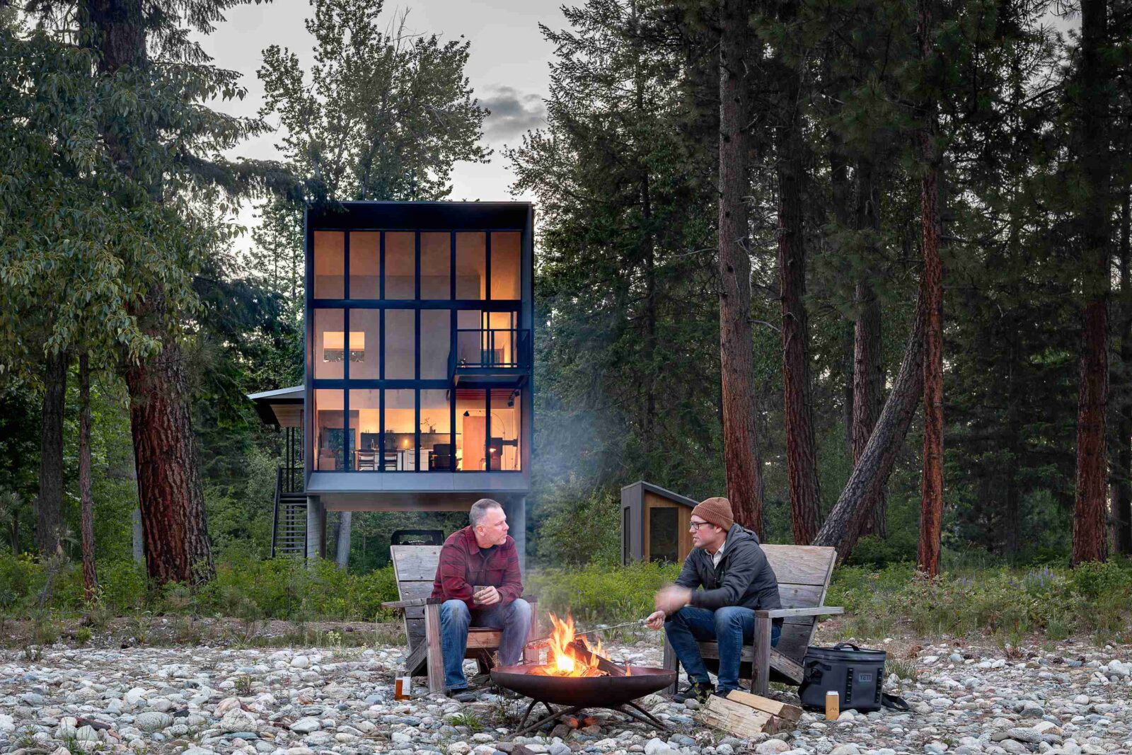 Wenatchee River Cabin by Wittman Estes. Client and architect by a fire in front of the house.