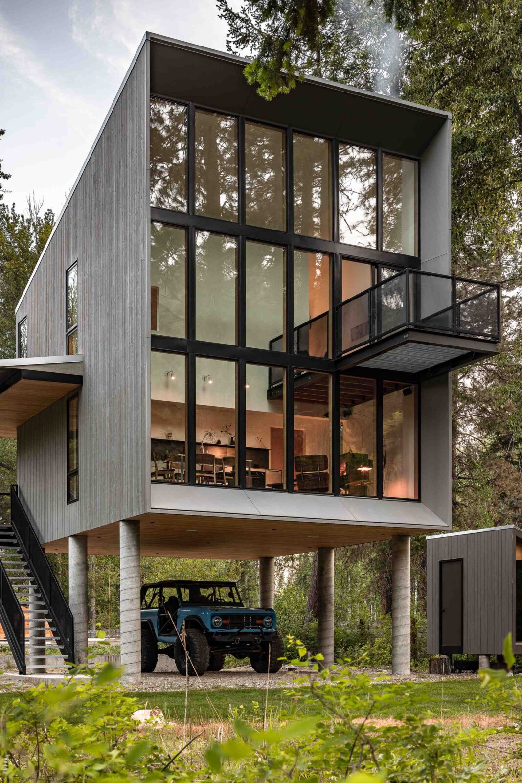 Wenatchee River Cabin by Wittman Estes. Outside façade with lights on and car below.