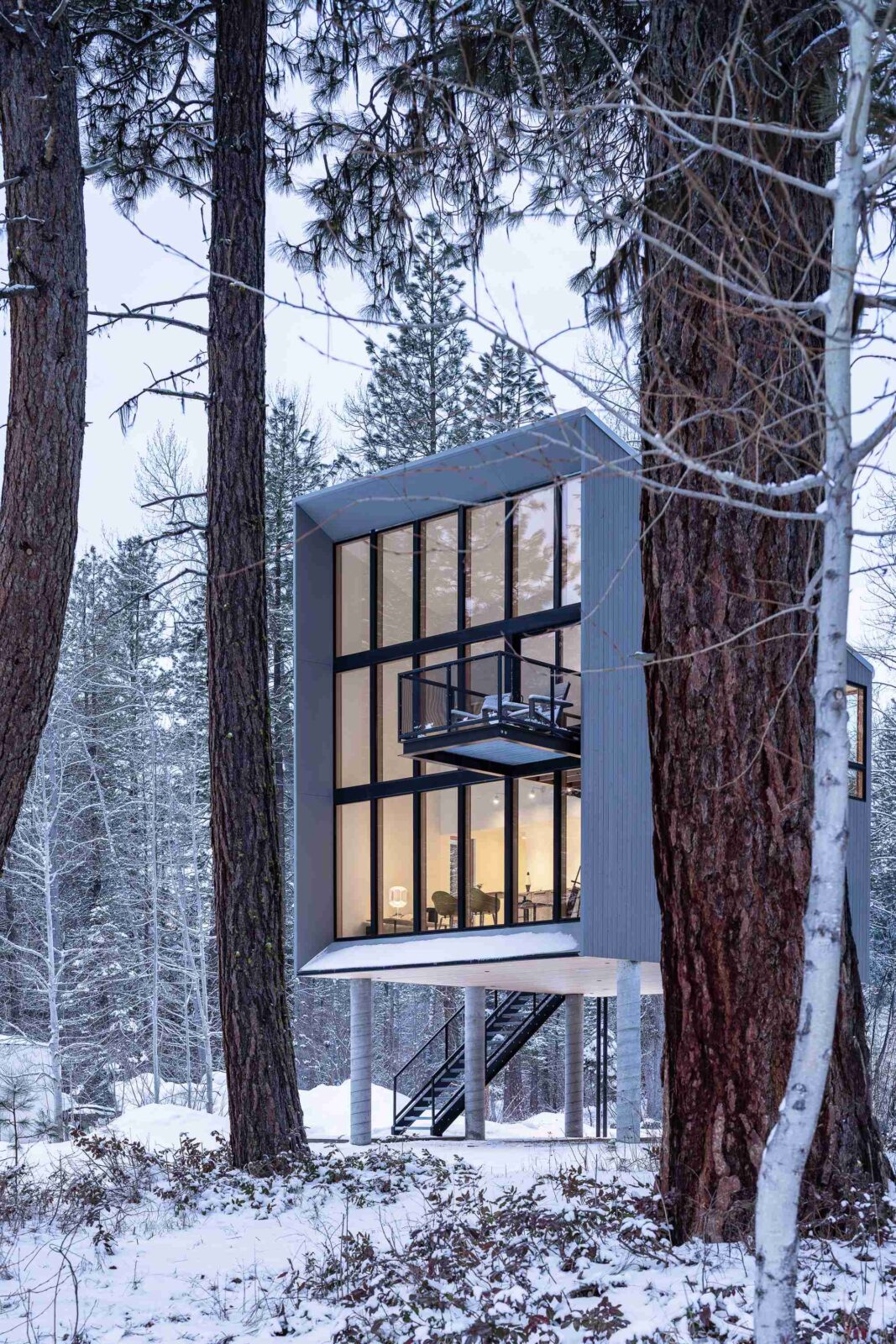 Wenatchee River Cabin by Wittman Estes. View of the façade with lights on in the snow.
